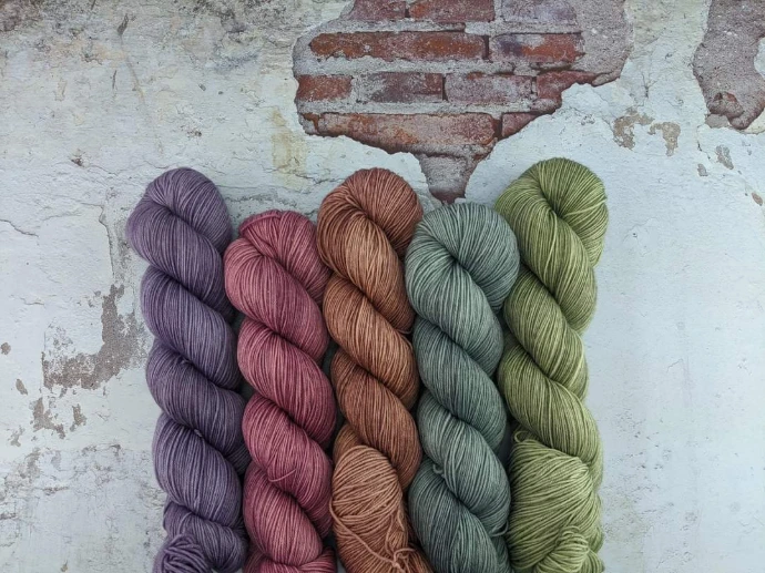 Hand-dyed yarn skeins in the Dystopian color palette, featuring muted purple, dusty rose, rust, slate blue, and olive tones.